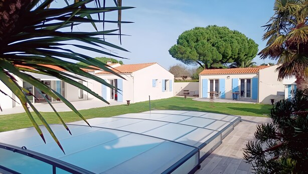 A residential area with a swimming pool, white houses with blue shutters, and a large tree.