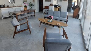A spacious living area with a dining table, sofa, and chairs, a ceiling fan, and large windows.
