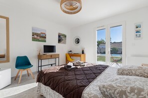 Ein Schlafzimmer mit einem Bett, einem Schreibtisch, einem Stuhl, einem Fernseher und Blick ins Freie.
