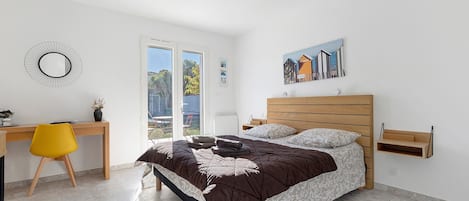 A bedroom with a bed, a desk, a chair, a window, and a wall-mounted shelf.