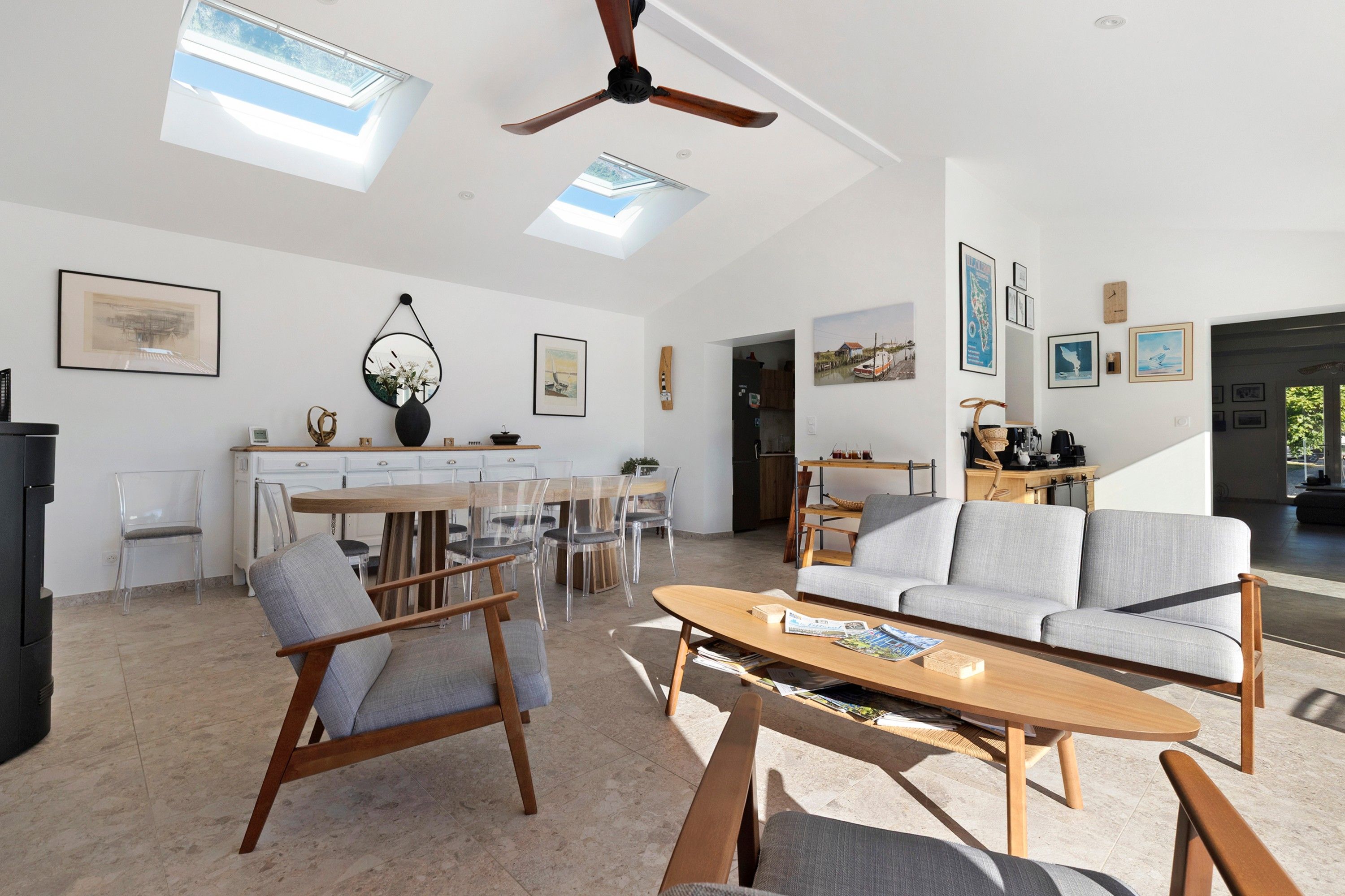 Un vaste espace de vie agrémenté d’un ventilateur de plafond, d’une table à manger avec des chaises, d’un canapé et d’œuvres d’art accrochées aux murs.