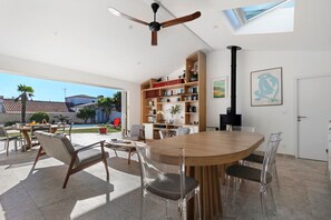 A spacious living area with a wooden dining table, clear chairs, a bookshelf, and a ceiling fan. - Bed and Breakfast 'Suite Les Plages' with Shared Pool, Shared Garden and Wi-Fi (La Brée-les-Bains)