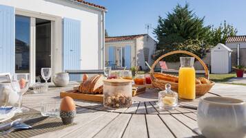 Un petit-déjeuner en plein air, avec du pain, des œufs et des boissons, disposé sur une table en bois.