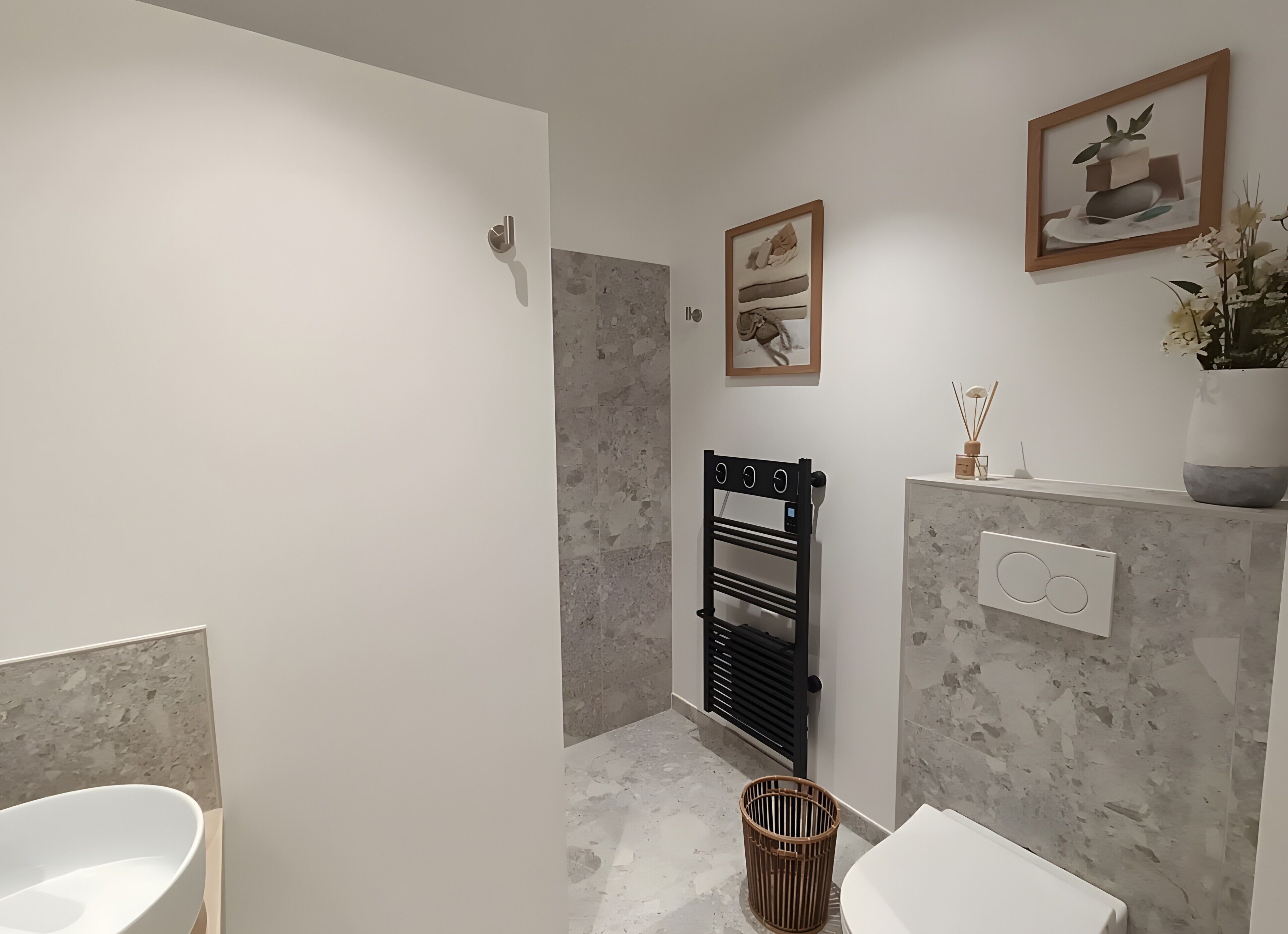 A modern bathroom with a white sink, a black towel rack, a white toilet, and a wall-mounted towel warmer.