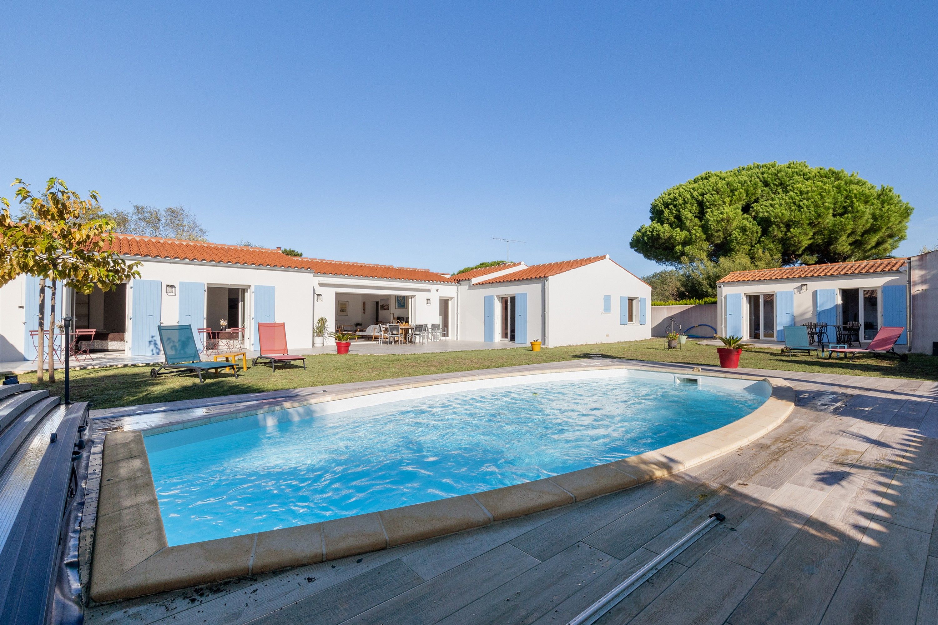 Vue sur une propriété résidentielle depuis la piscine, avec piscine, espace salon extérieur et un grand arbre.
