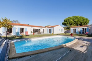 A poolside view of a residential property with a swimming pool, outdoor seating, and a large tree. - Bed and Breakfast 'Suite Les Plages' with Shared Pool, Shared Garden and Wi-Fi (La Brée-les-Bains)