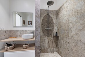 Une salle de bain moderne avec un lavabo sur pied, un miroir et une douche dotée d’un pommeau de douche incurvé.