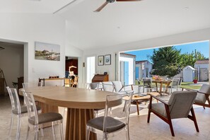 A spacious dining area with a large wooden table surrounded by chairs, a kitchen area with a wooden cabinet, and a view of the outdoors. - Bed and Breakfast 'Suite Les Plages' with Shared Pool, Shared Garden and Wi-Fi (La Brée-les-Bains)
