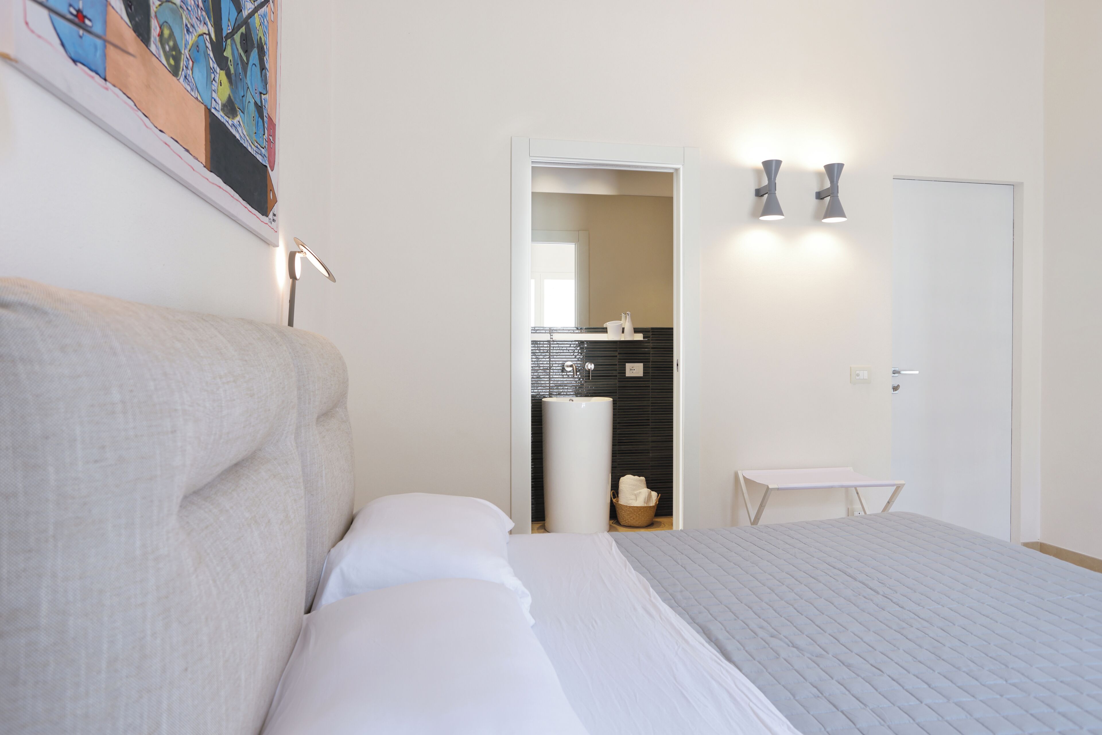 Een slaapkamer met een bed, een nachtkastje, een wandlamp, een deur en een zichtbare badkamer door een open deur.