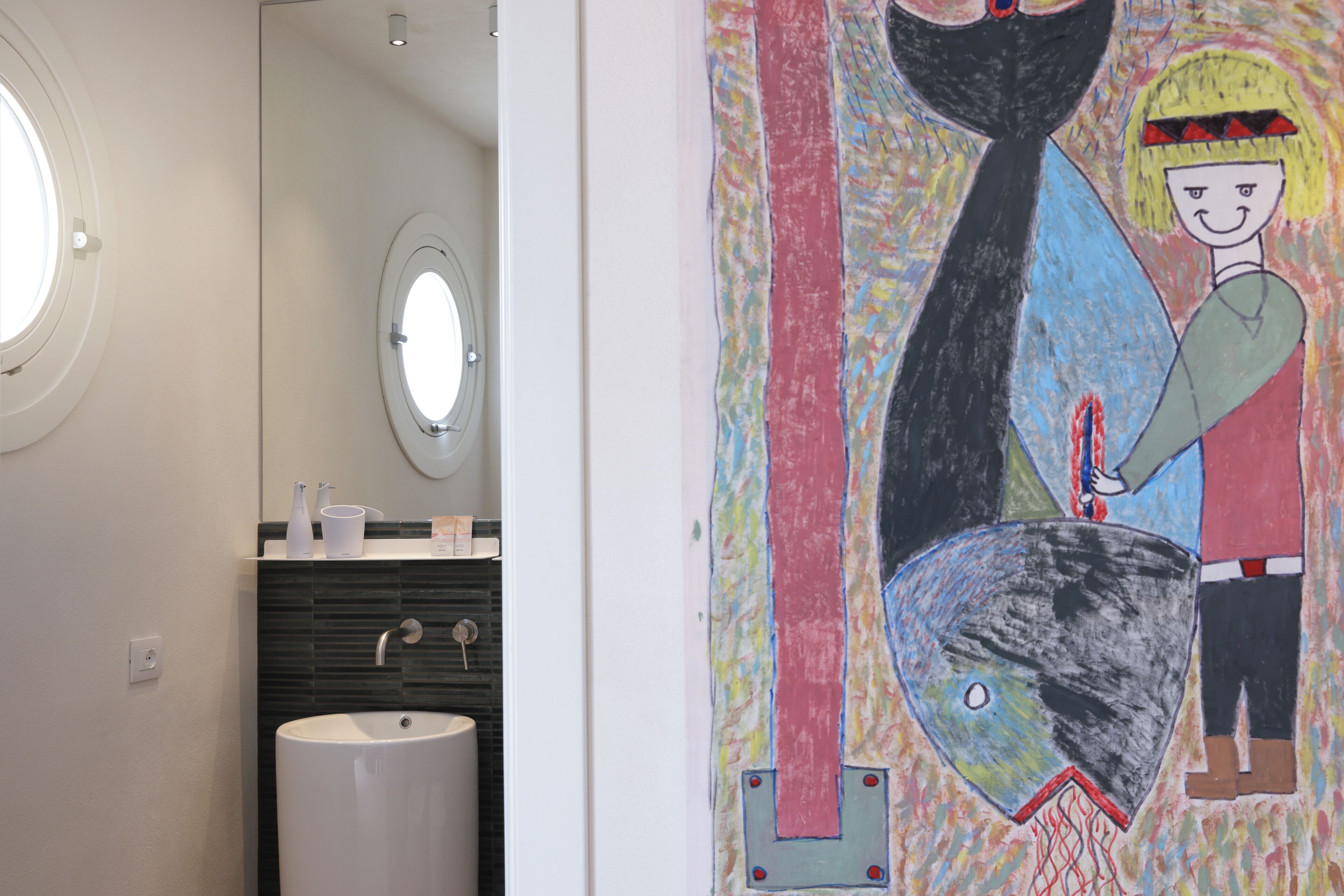 Un bagno con un lavandino bianco, uno specchio e un quadro astratto colorato appeso alla parete.