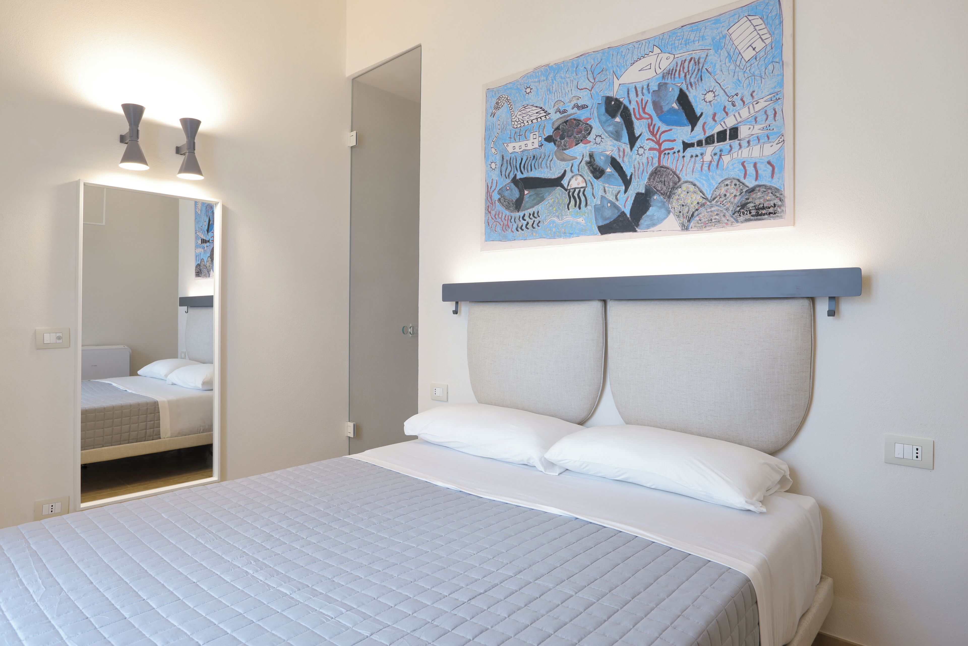 Ein Schlafzimmer mit Bett, Kopfteil, Wandbild und Spiegel.