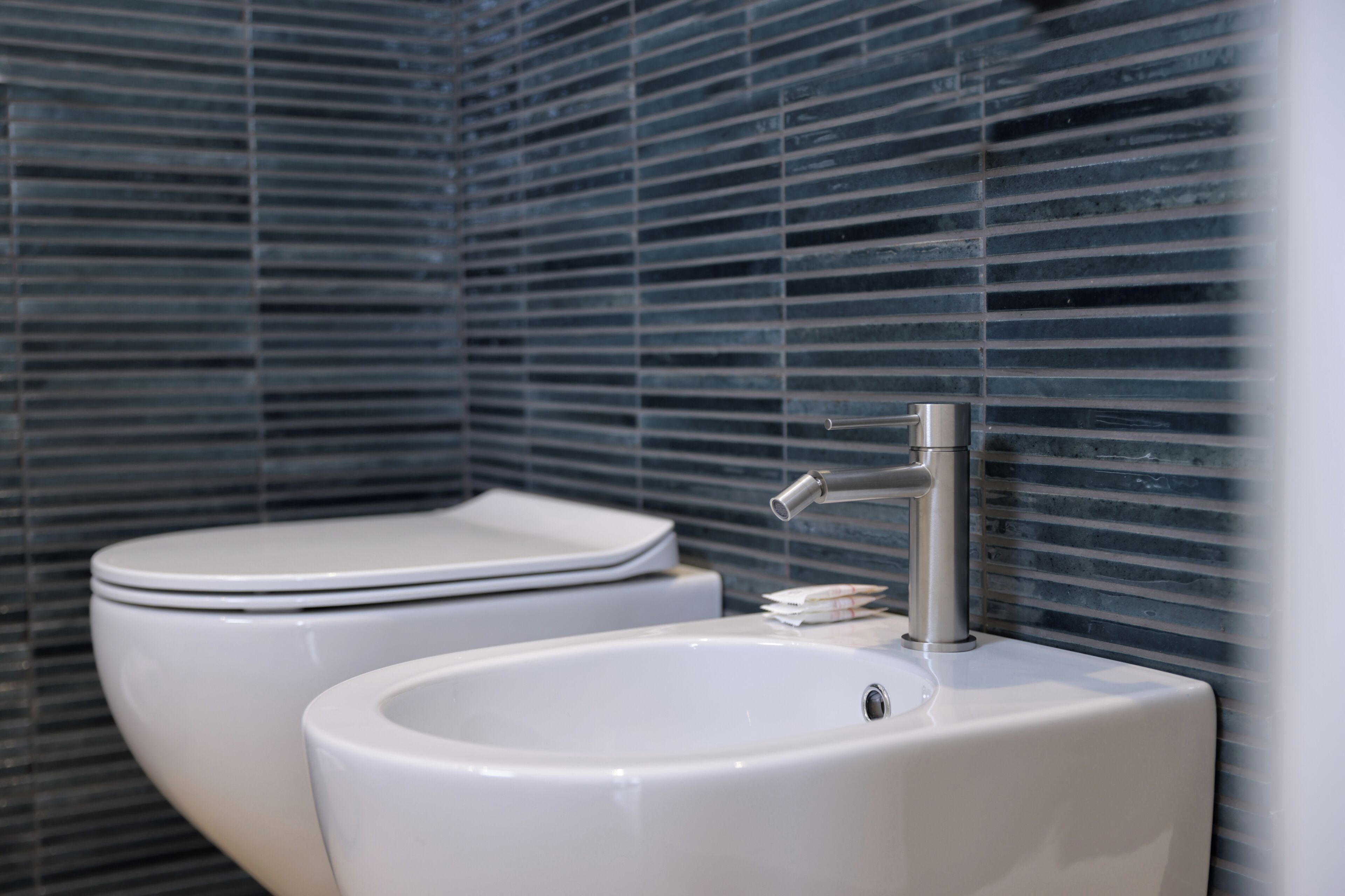 Une salle de bain avec des toilettes et un lavabo, tous deux de couleur blanche, devant un mur carrelé.
