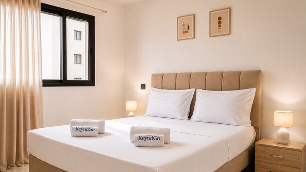 A hotel room with a bed, two bedside lamps, a nightstand, a window with curtains, and two framed pictures on the wall. - Sandra 28 (Tunis)