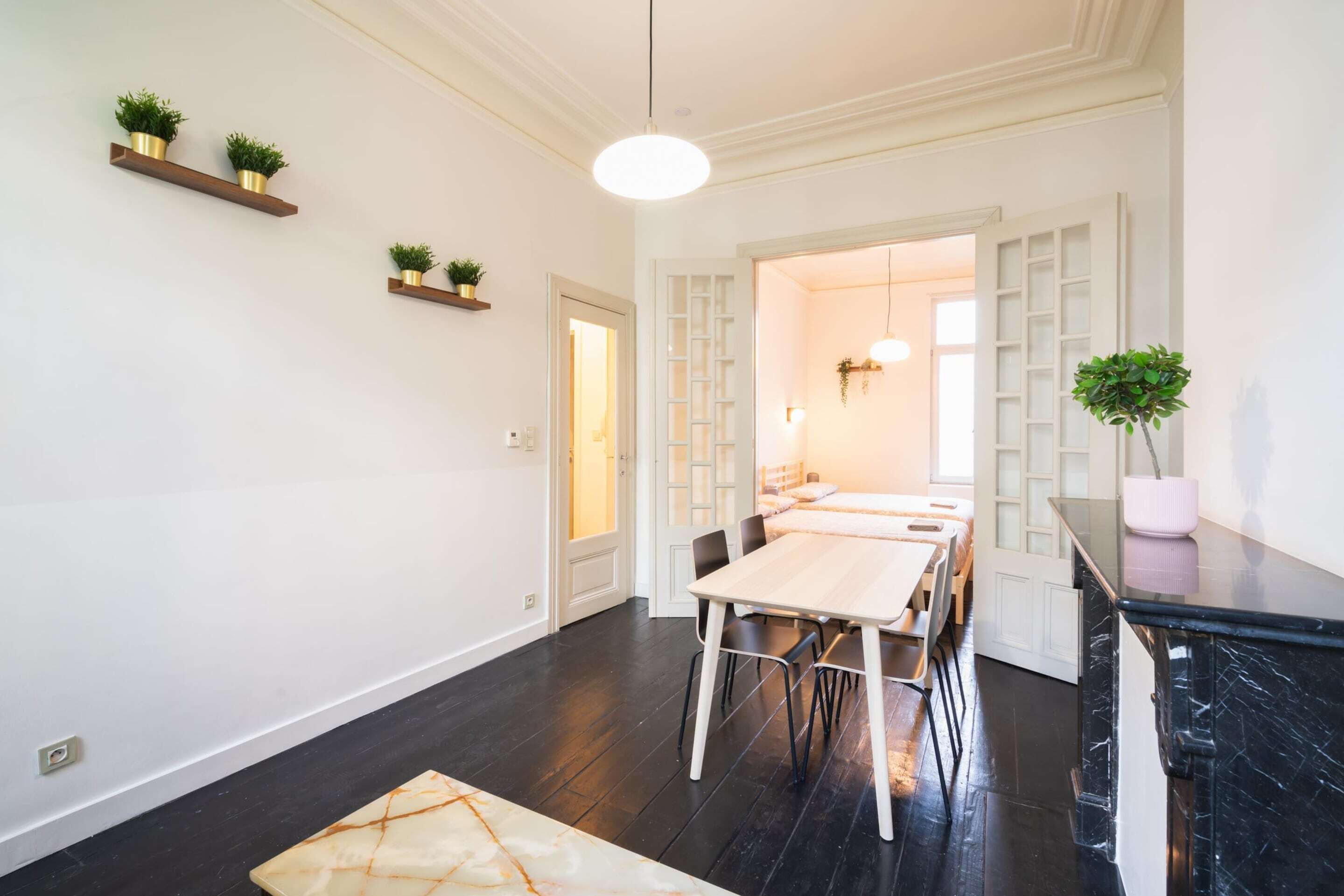 Um interior moderno com área de jantar, piso de madeira escura e estantes embutidas com plantas.