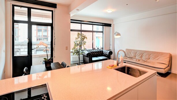 A modern kitchen with a central island, a dining area with a black leather sofa, and a view of the street through large windows. - Spacious Apartment in Heart of Antwerp (Antwerp)