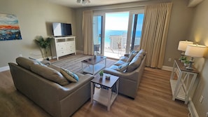 Ein Wohnzimmer mit Sofa, Couchtisch, Fernseher und einem Balkon mit Vorhängen.