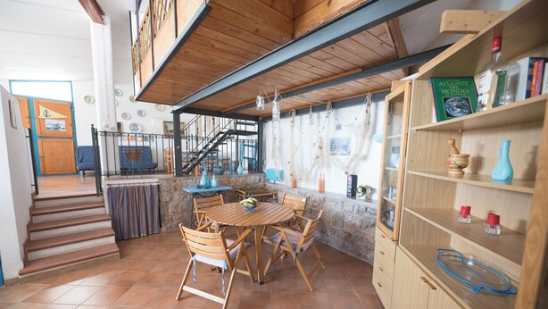 A dining area with a wooden table and chairs, a staircase, and a bookshelf with various items. - Grandparents' Shelter between Sky and Sea (Lazio)