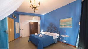 A bedroom with a bed, a bedside table, a lamp, a painting, and a chandelier. - Grandparents' Shelter between Sky and Sea (Lazio)