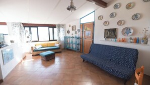A living room with a sofa, a bench, a dining table, and a kitchen area. - Grandparents' Shelter between Sky and Sea (Lazio)