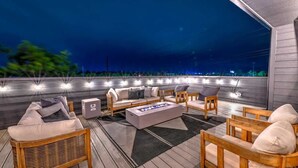 Un espacio exterior con mobiliario de mimbre, una fogata y luces colgantes.