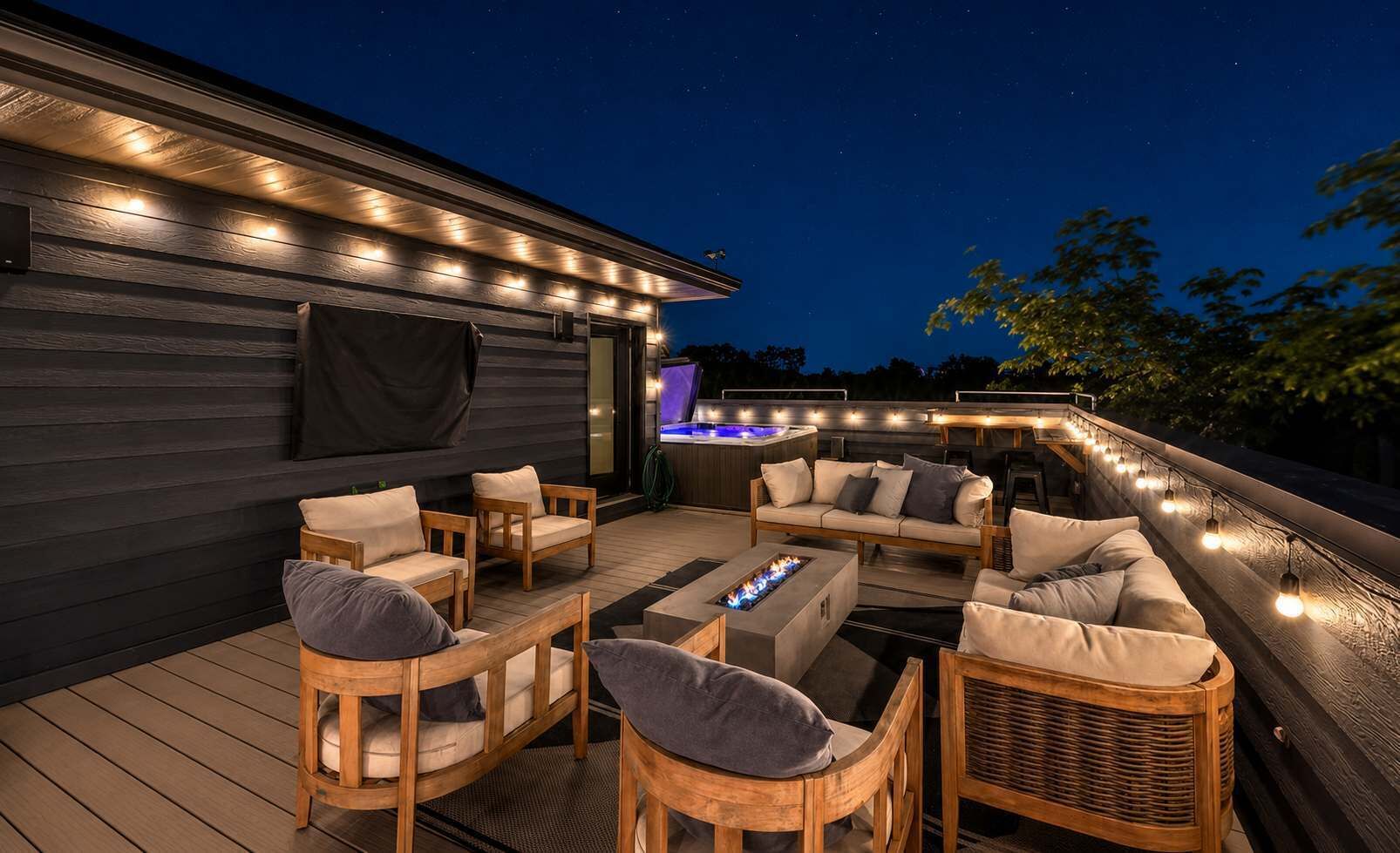 Une terrasse extérieure avec des meubles en bois, un foyer et des guirlandes lumineuses.