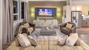 Een moderne woonkamer met een grote flatscreen televisie, twee banken, een salontafel en een keuken op de achtergrond.