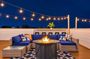 An outdoor seating area with a fire pit, string lights, and a view of the city skyline. - Lux Nash Experience | Fire Pit + Game Room 9 Beds (Nashville)