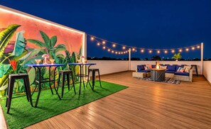 Een terras buiten met een tafel, stoelen, een bank en sfeerverlichting.