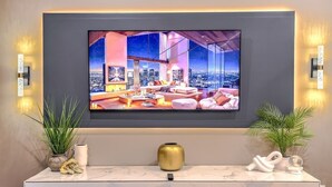 Een moderne woonkamer met een grote televisie, een marmeren console en decoratieve planten.