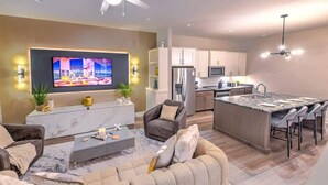Een moderne woonkamer met een grote televisie, een bank, een salontafel en een eethoek met stoelen.