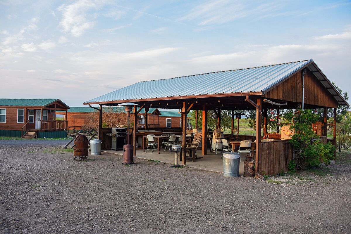 A rustic outdoor seating area with a metal roof, wooden tables, and chairs.