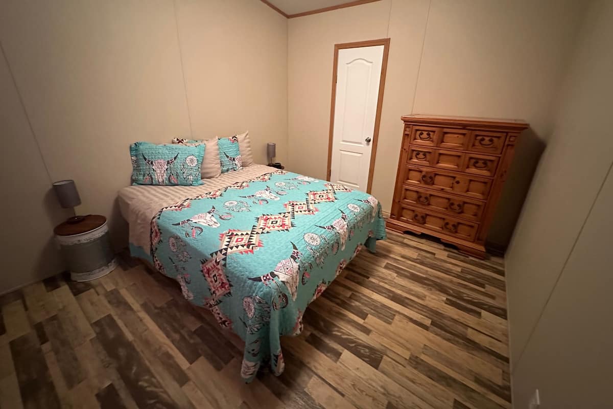Un dormitorio con una cama, un aparador de madera, un cubo de basura y una puerta.