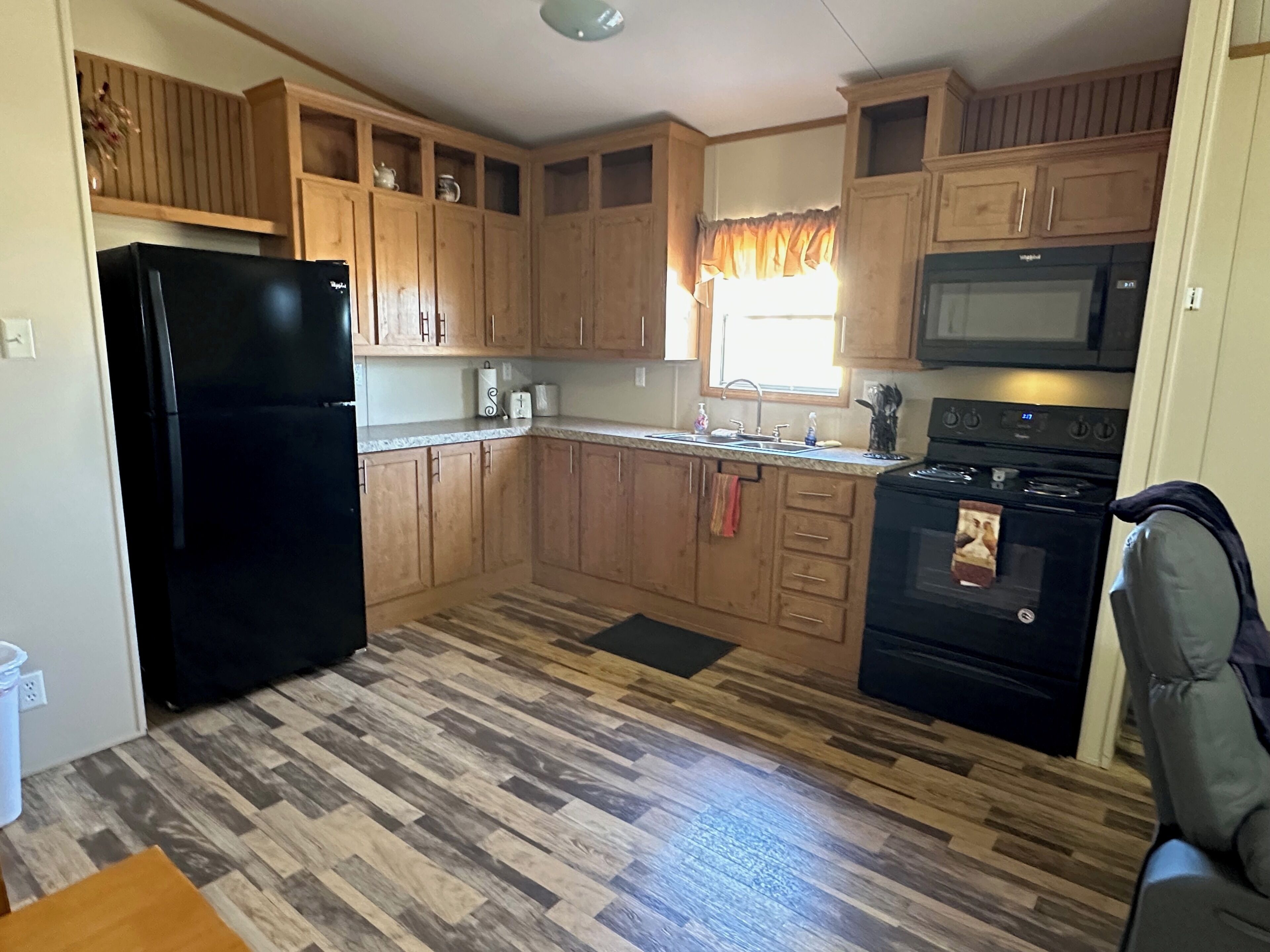 A compact kitchen with wooden cabinets, a black refrigerator, a microwave, and a stove.