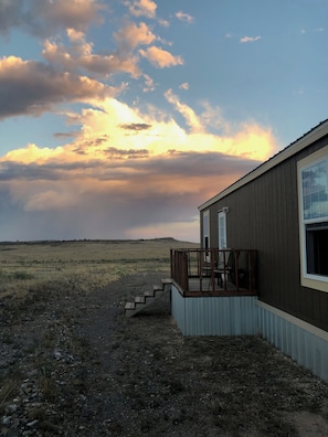 A building with a deck and a window, set against a rural landscape with a cloudy sky.