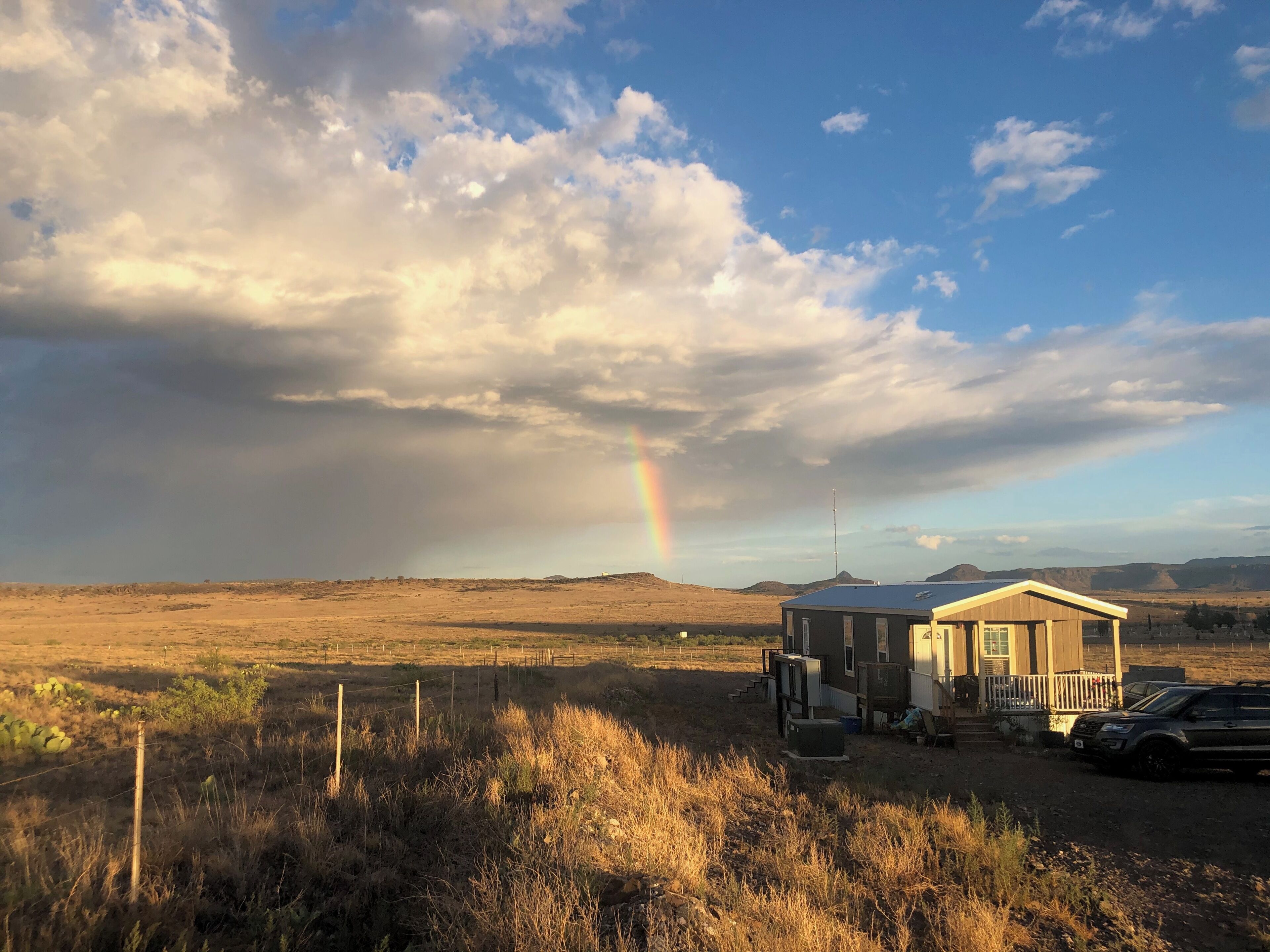 A rural landscape with a house, a rainbow, and a clear sky.