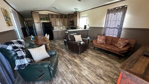 A spacious living area with a dining table, leather sofas, and a kitchen in the background.