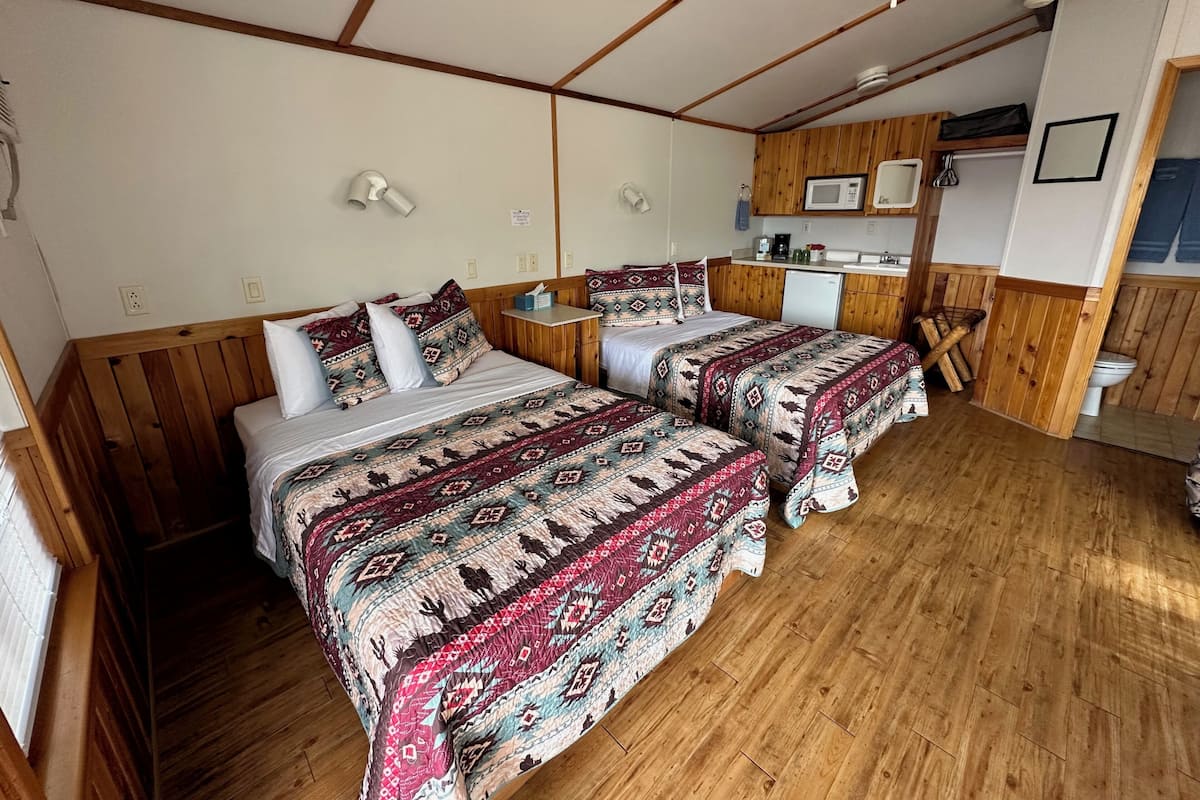 Una habitación con dos camas, paredes de madera, una kitchenette pequeña y un ventilador de techo.
