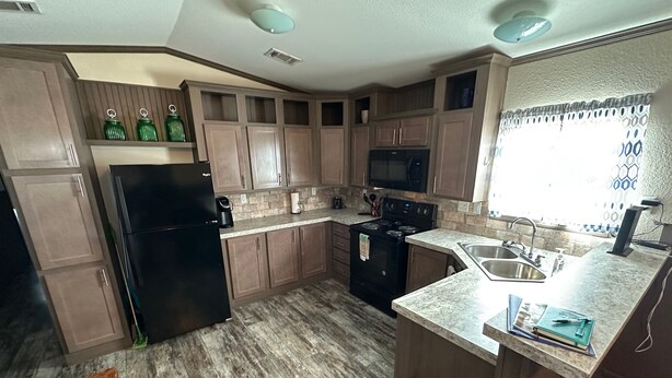 A kitchen with wooden cabinets, a black refrigerator, a stove, and a sink.
