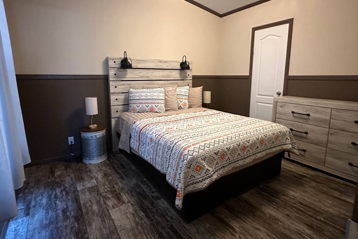 Un dormitorio con cama, lámparas de noche, cómoda y cubo de basura.