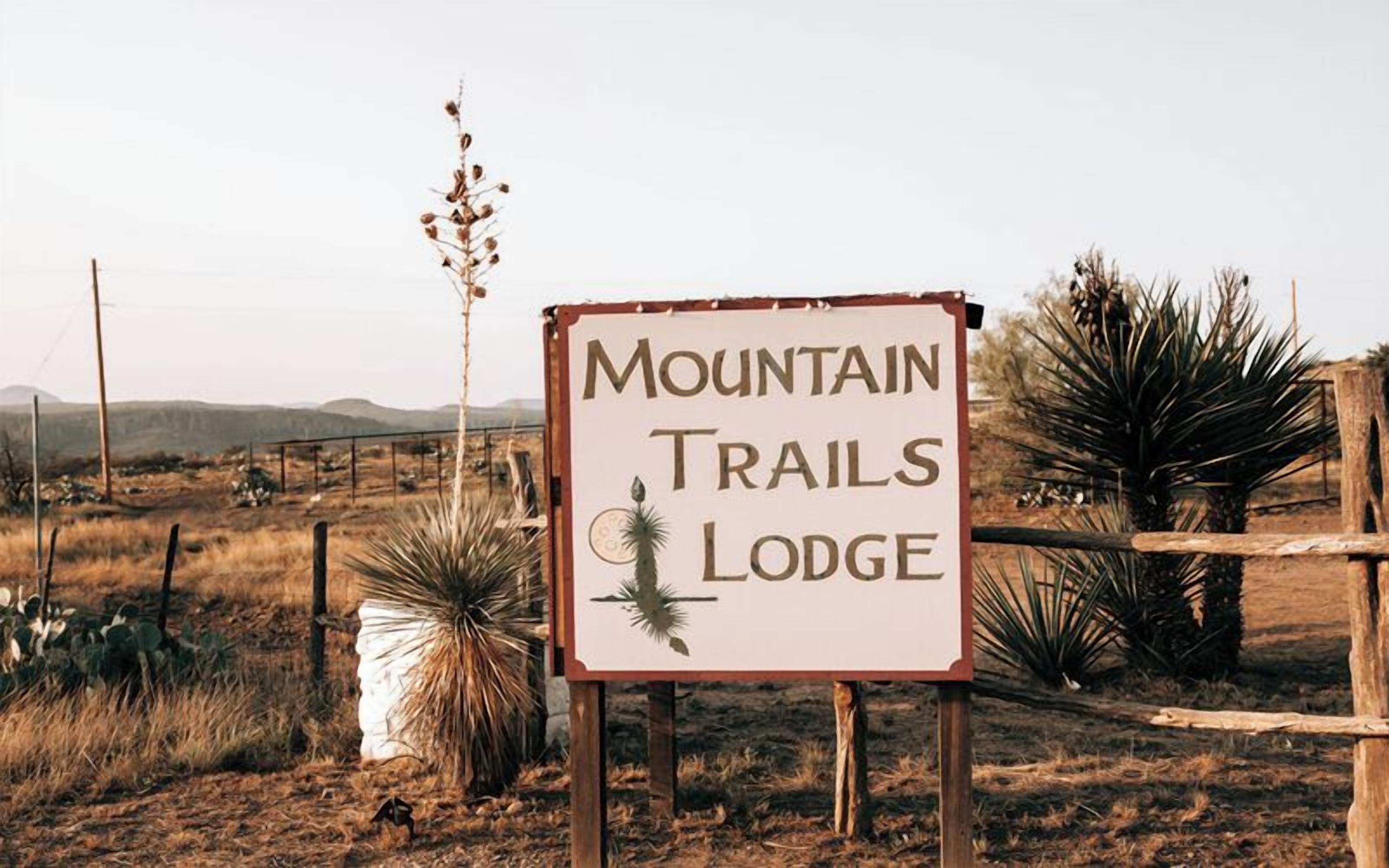 Naamplaatje voor Mountain Trails Lodge, met een cactus en woestijnlandschap op de achtergrond.