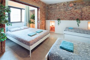 Ein Schlafzimmer mit Backsteinwand, einem Bett mit gemustertem Überwurf, einem Nachttisch und einem Fenster.