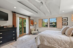 Ein Schlafzimmer mit Bett, Kommode, Fernseher, Sessel und einem Fenster mit Blick.