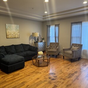 Ein Wohnzimmer mit einem dunkelgrauen Sofa, zwei Sesseln, einem Glastisch und einer dekorativen Vase.