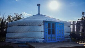 A yurt with a blue door, a chimney, and a deck.