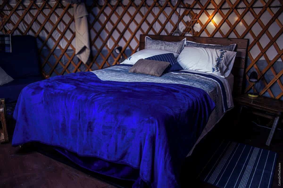 Una cama con manta azul, cabecero de madera y varios almohadones.