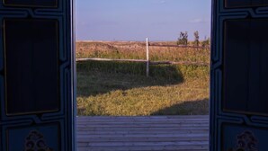 An open door leading to a view of a grassy field with a fence and a wooden deck.