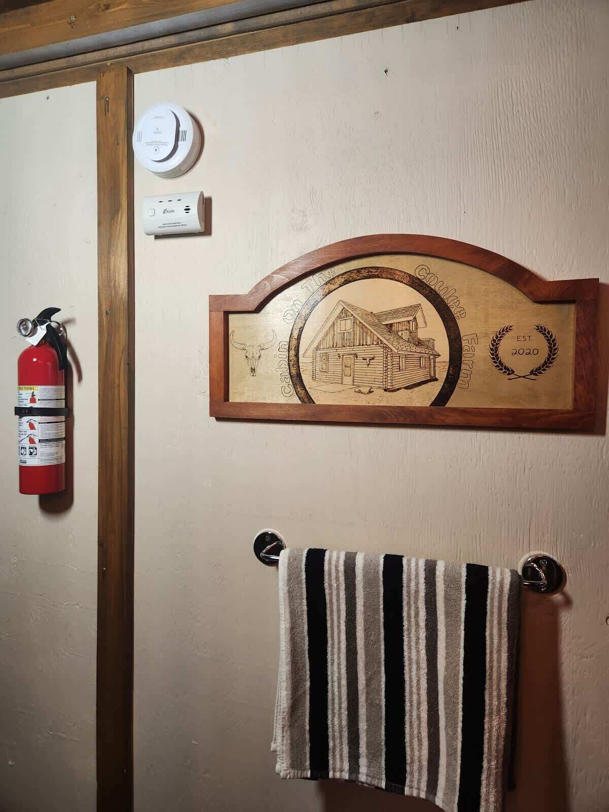Un élément de décoration murale en bois, représentant une illustration de grange, un extincteur et un porte-serviettes avec une serviette à rayures.