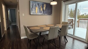 Een eetgedeelte met een tafel, stoelen, een hanglamp en een schilderij aan de muur.