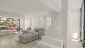En moderne stue med en grå hjørnesofa, et hvidt sofabord og en trappe med glasgelændere.