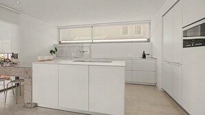 Et moderne køkken med hvide skabe, en stor køkkenø og en indbygget ovn.